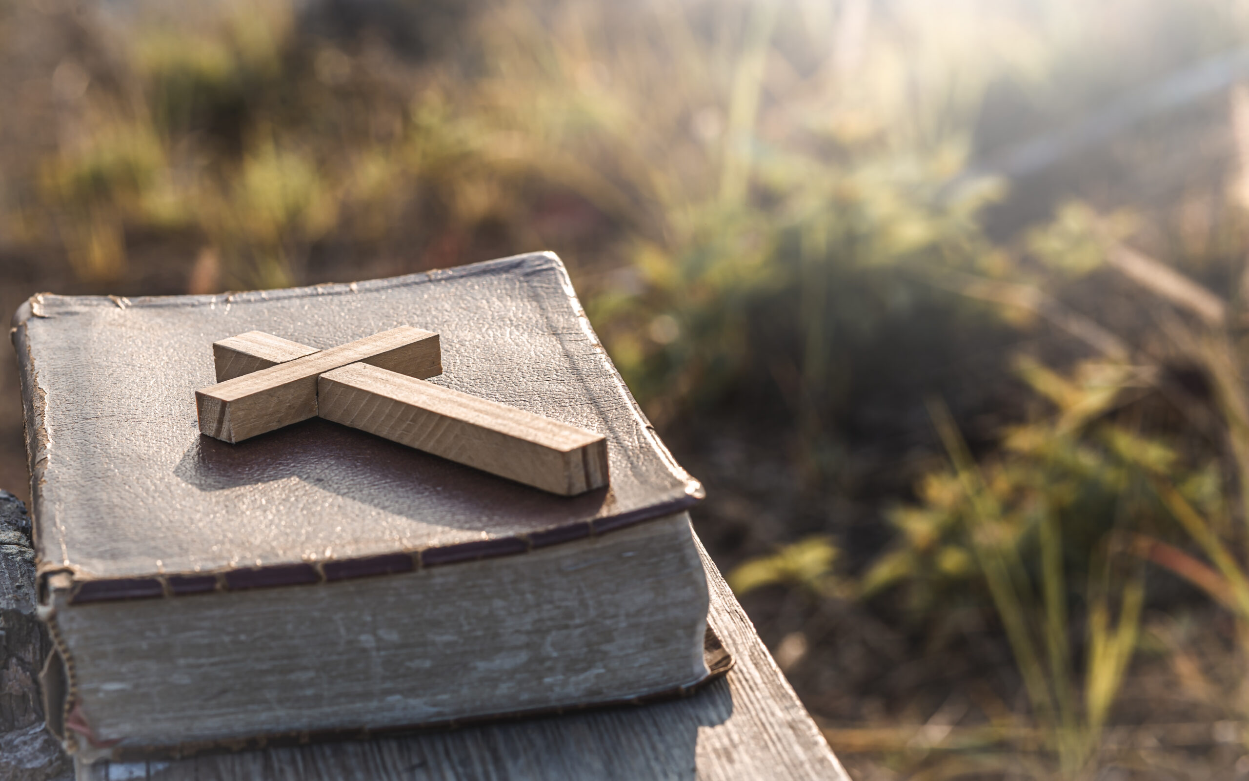 The Cross with old Bible lay on wooden plate, christian concept.